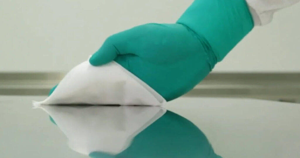 compounding pharmacist with a gloved hand using a hydroflex cleanroom wipe