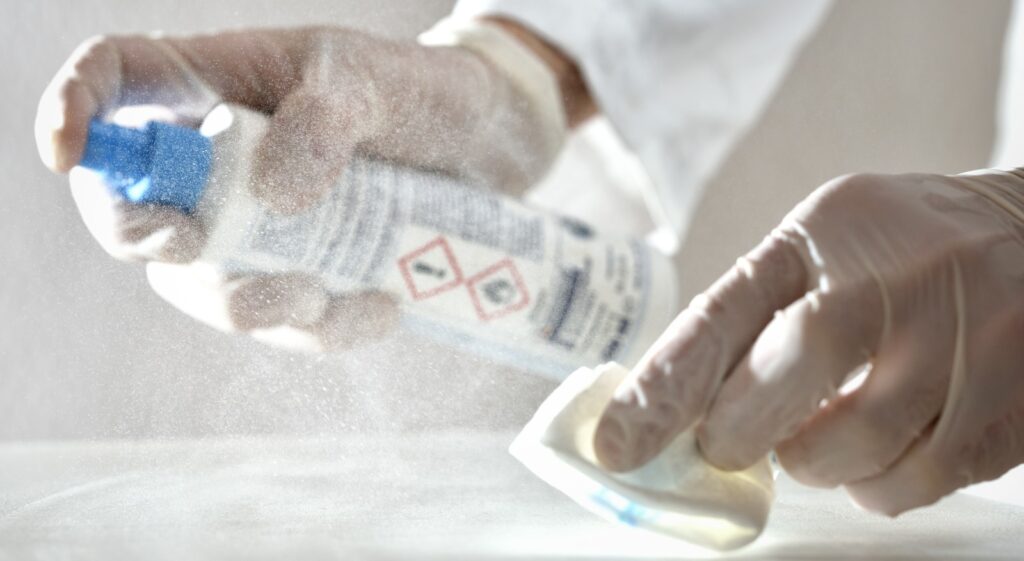 cleanroom worker spraying disinfectant on surface while using a cleanroom wipe