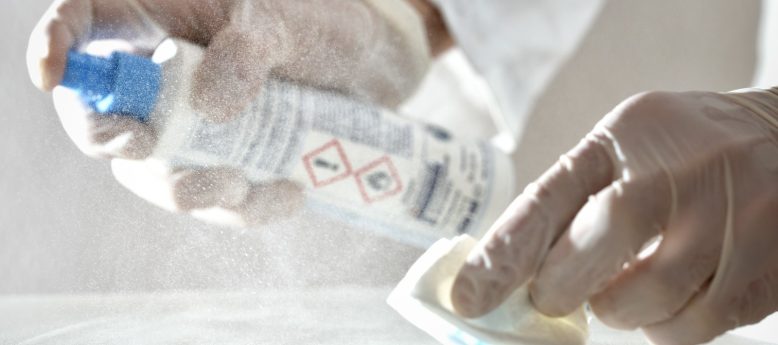 cleanroom worker spraying disinfectant on surface while using a cleanroom wipe